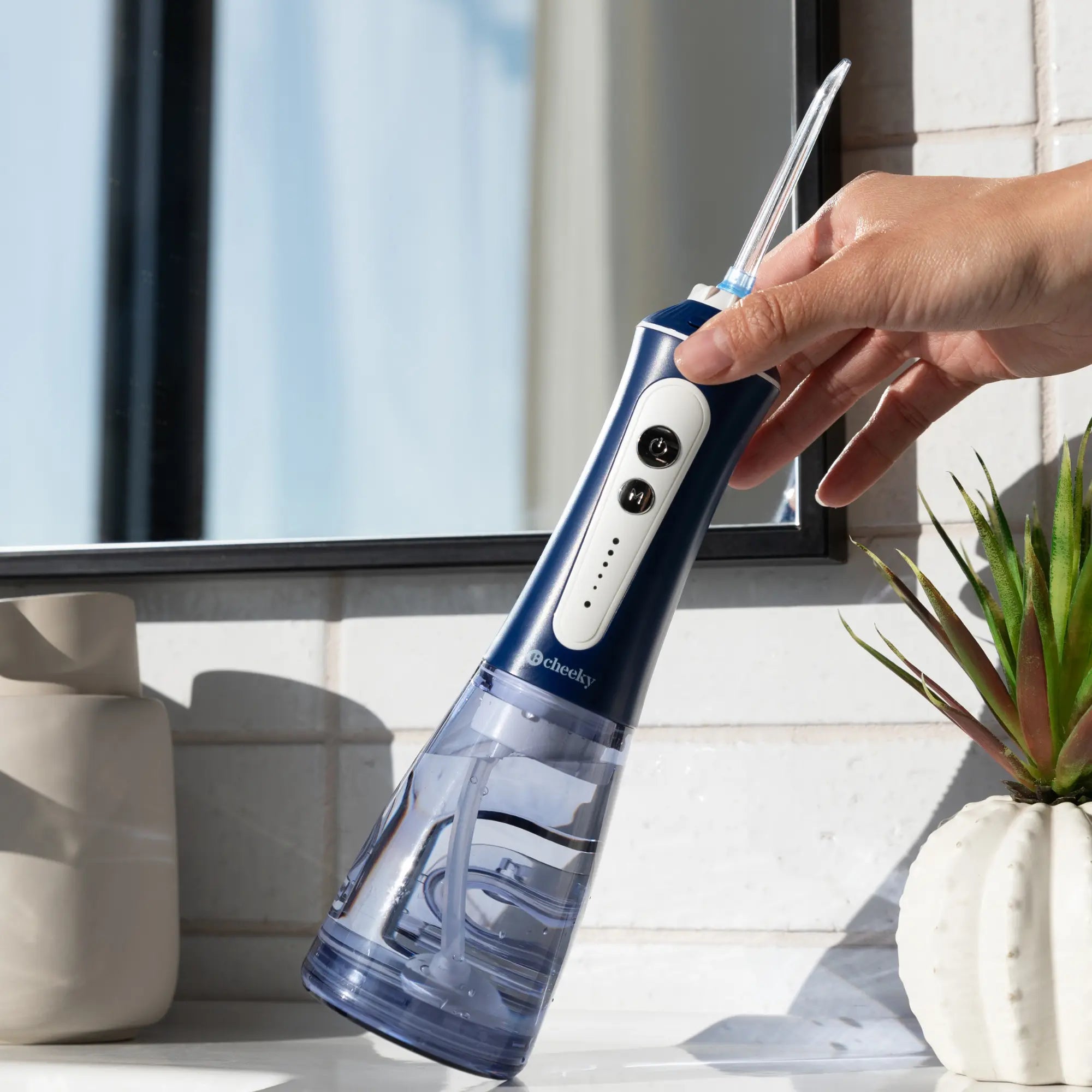 Hand holding a blue and white dental water flosser with a blurred indoor background