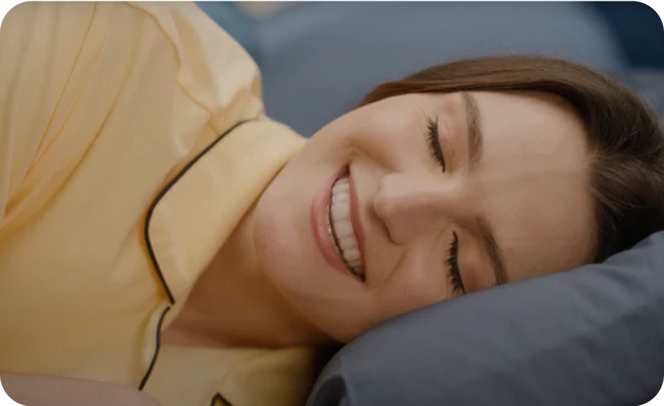 A woman lays in bed with a bright smile-Cheeky